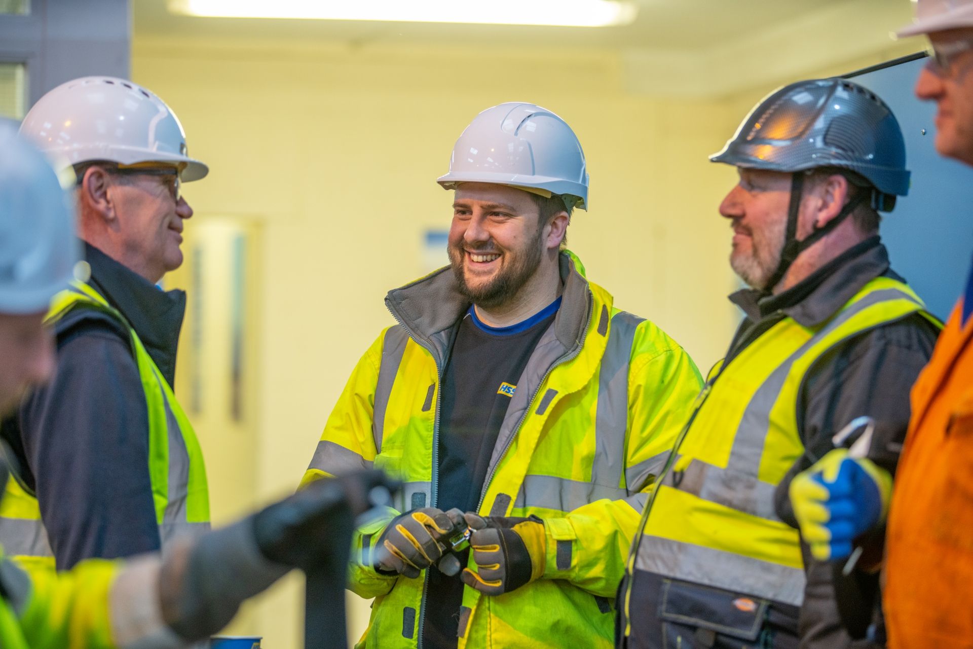 5 people having a conversation, all wearing hard hats and hi vis